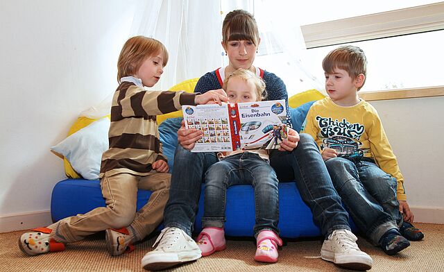 Erzieherin liest drei kindern Buch vor