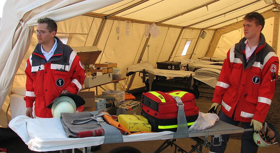 zwei Rettungssanitäter im Rettungszelt mit vorbereiteter Lieg