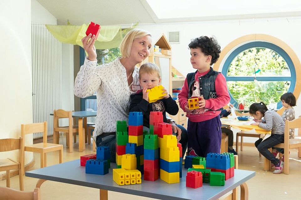 Erzieherin spielt mit zwei Kindern und Bauklötzen