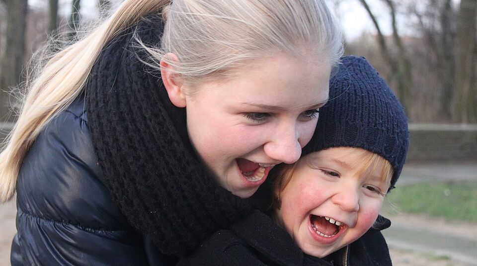 ein kleines Kind und eine Jugendliche lachen zusammen