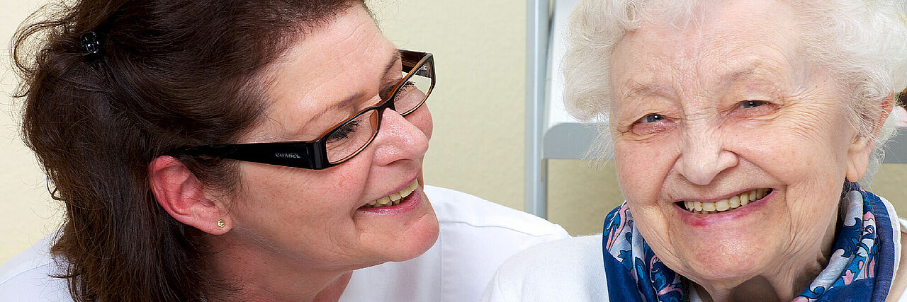 Pflegerin mit Seniorin Die Pflegerin lächelt die Seniorin an