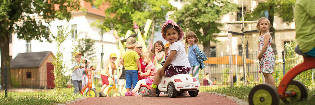 Kinder auf Bobbycars im Kita Garten