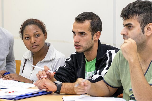 vier Menschen sitzen zusammen vor DRK Mappen und diskutieren