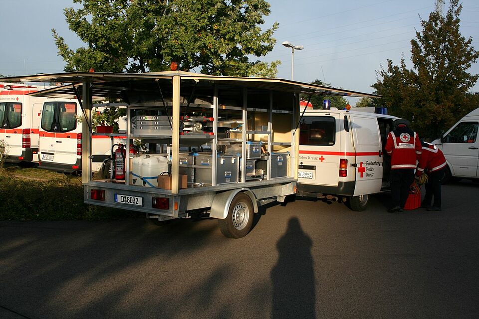 geöffneter technischer Anhänger mit DRK Autos in Abendsonne