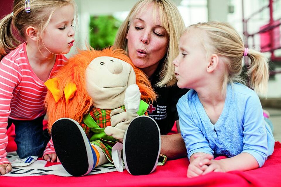 zwei Kitakinder und eine Erzieherin spielen mit Handpuppe