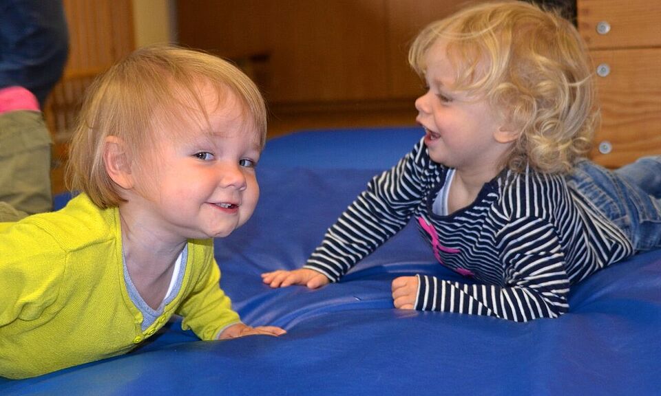 zwei lachende und krabbelnde Babys auf einer blauen Sportmatte